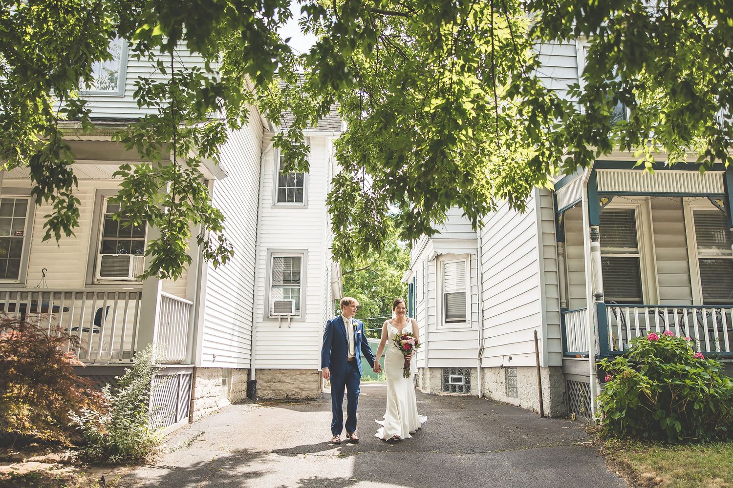 Tree-lined residential street with white houses provides romantic wedding backdrop.
