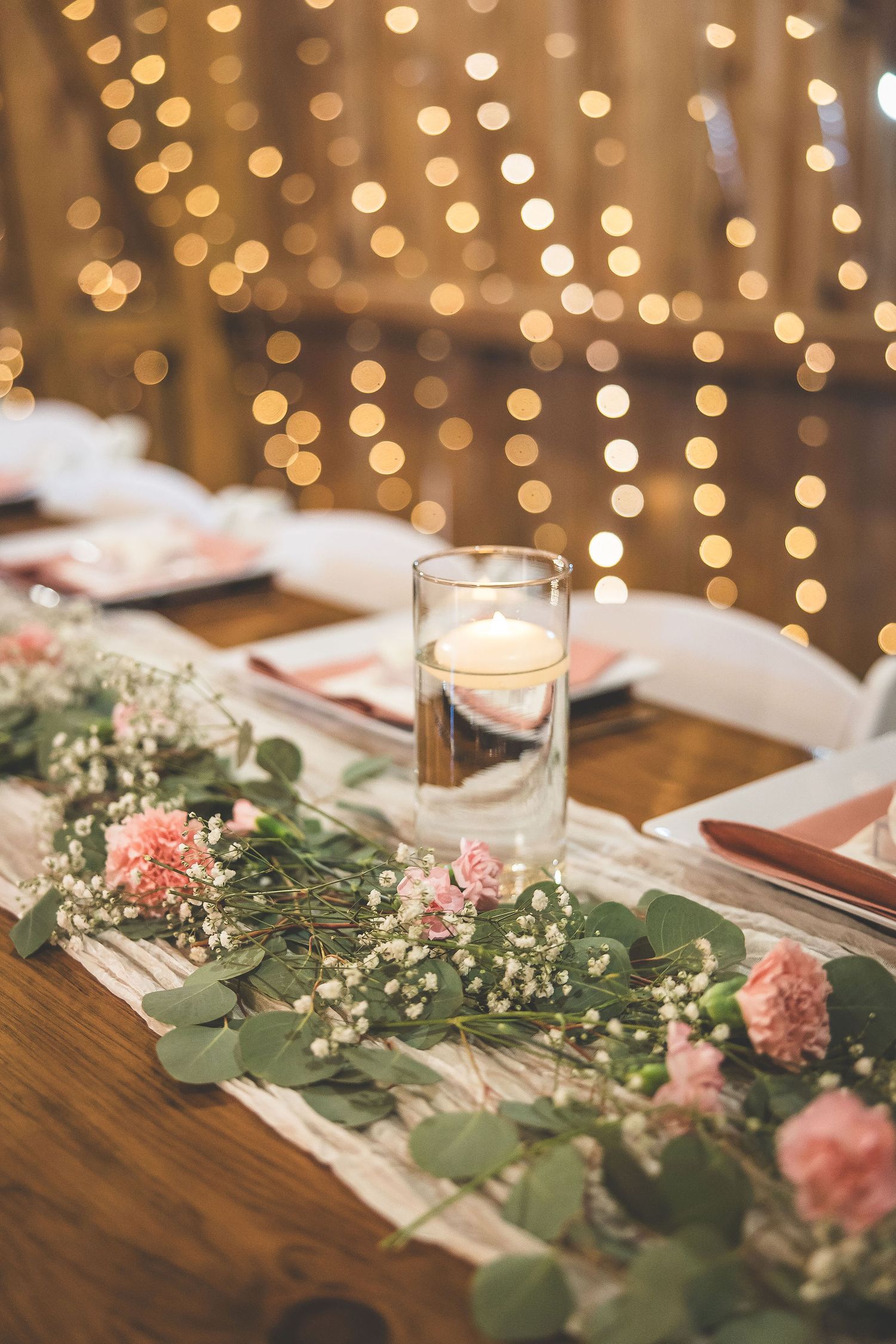Romantic table setting with floating candles and pink floral garland against bokeh lights.