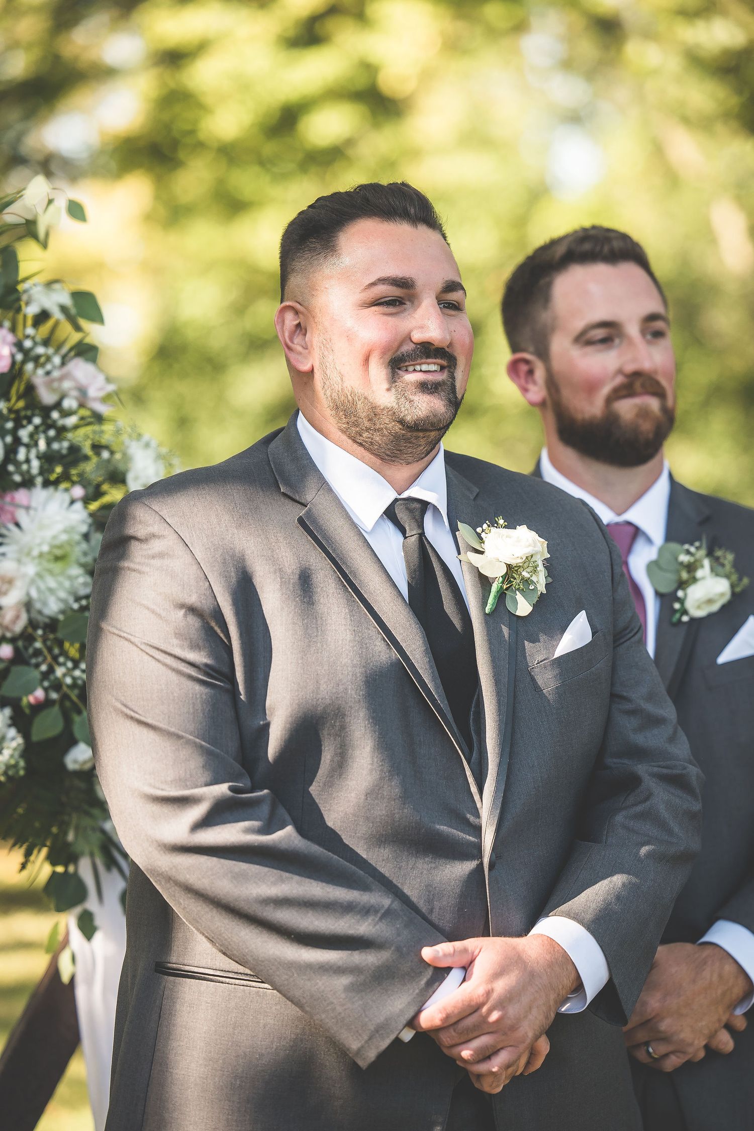 Groomsmen in brown suits standing together during an outdoor wedding ceremony.
