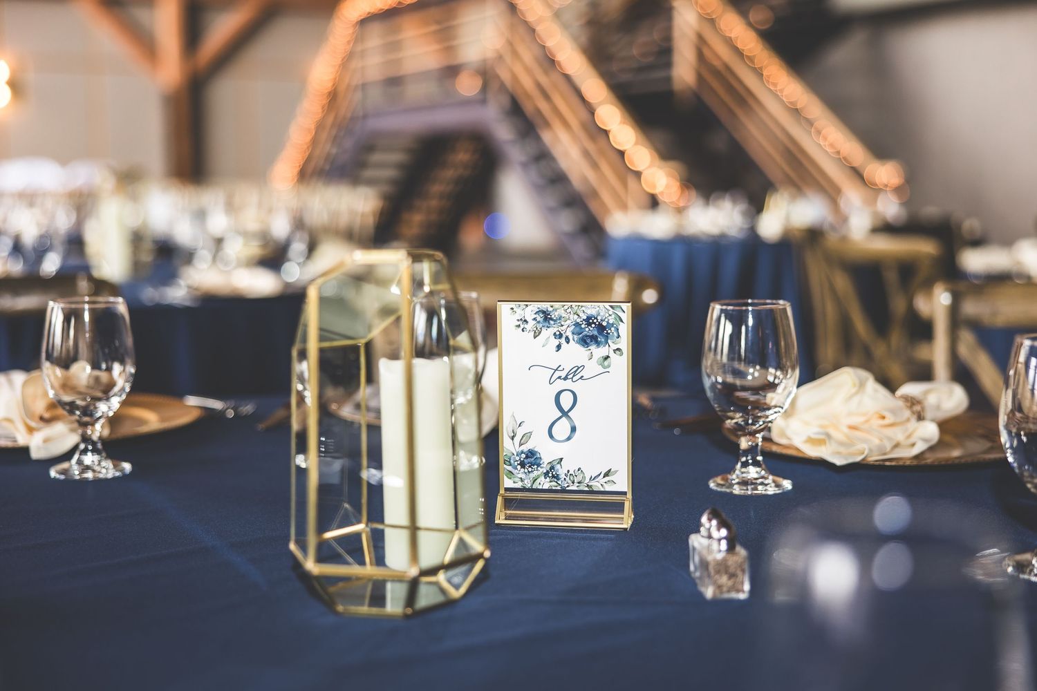 Wedding table setting with geometric candle holders, table numbers, and navy blue linens.