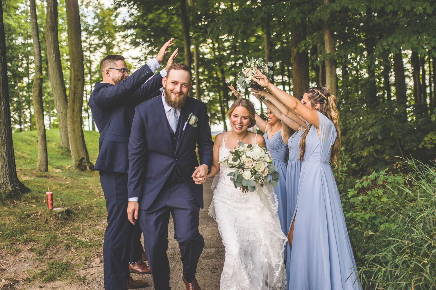 Wedding party celebrates joyfully on wooded path during outdoor photo session.