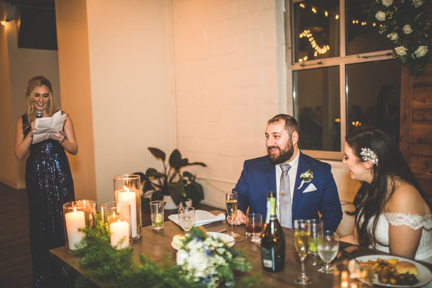 Intimate wedding reception dinner with candlelit tables and string lights overhead.