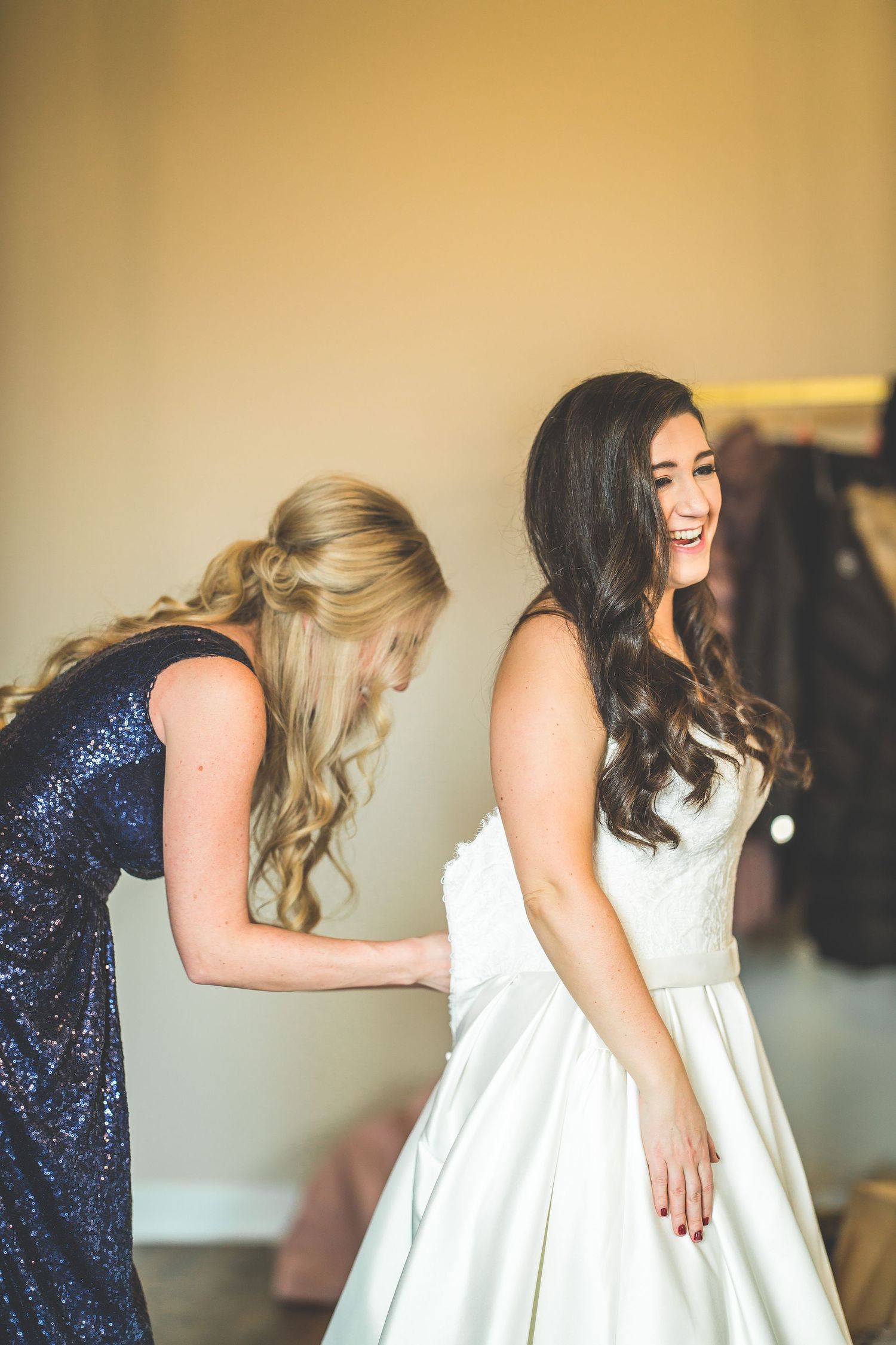 Wedding party members in navy sequins and white dresses share an animated moment of laughter.