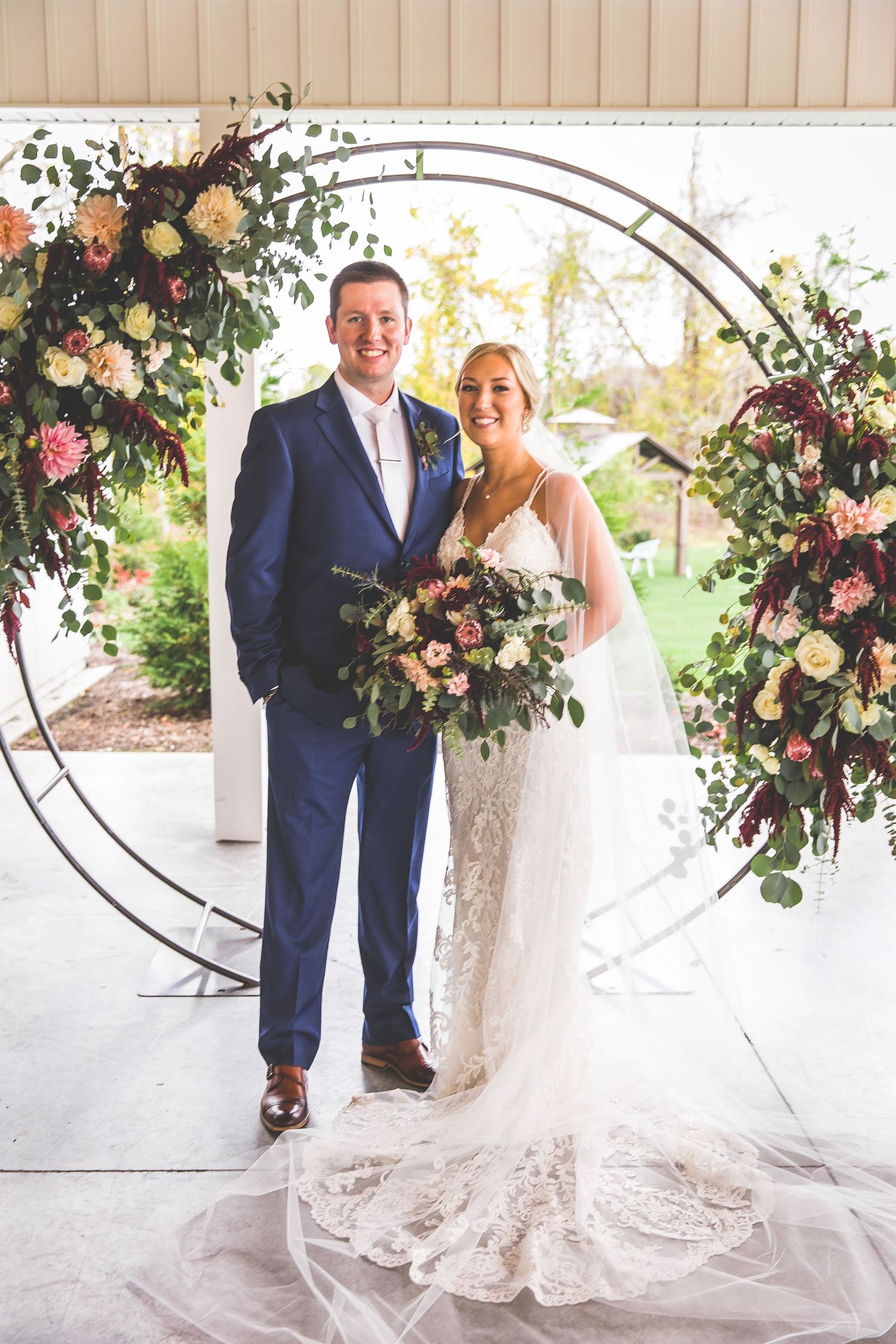 Wedding portrait in front of circular floral arch with peach and burgundy blooms.