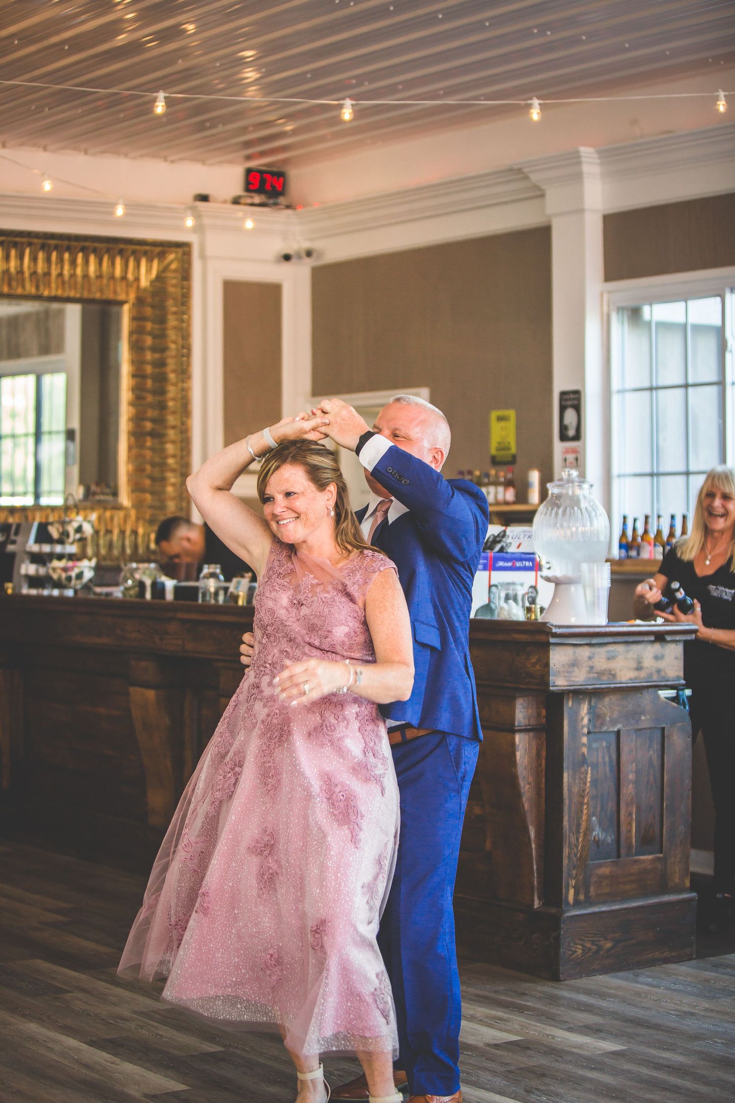 A couple dancing in formal attire, with the woman wearing a pink sparkly dress at a wedding reception.