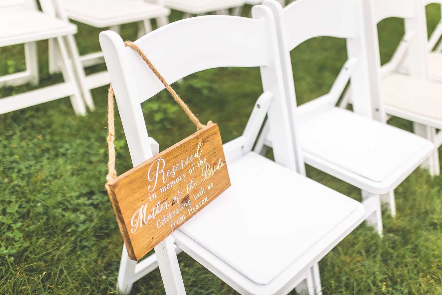 White folding chairs set up for outdoor wedding ceremony with wooden signs.