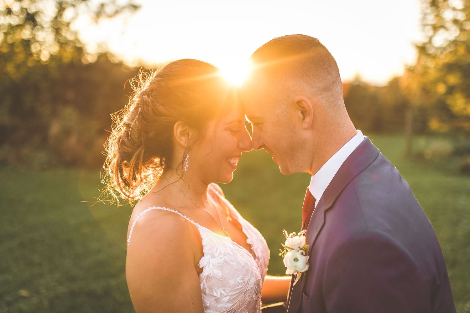 Romantic sunset wedding portraits show couple embracing in golden light across grassy field.