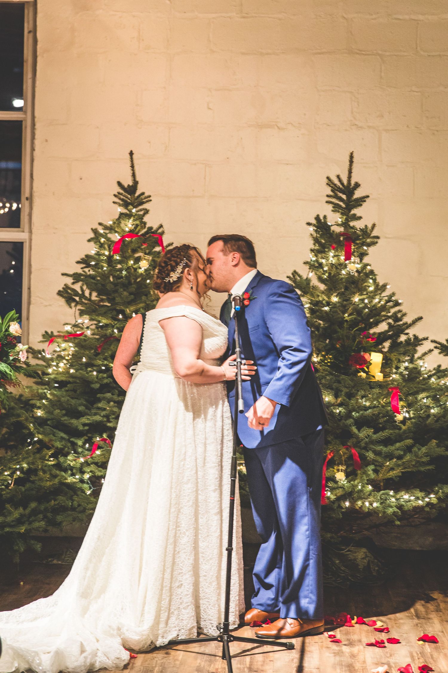 A couple shares their first dance in front of decorated Christmas trees at their winter wedding.
