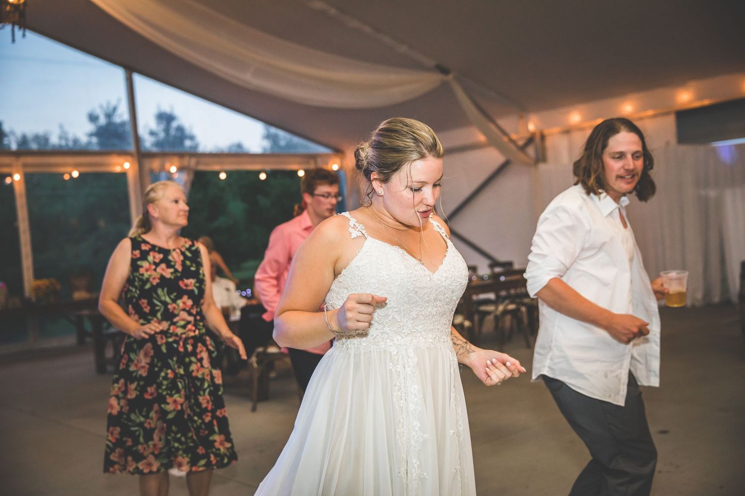 People dancing and celebrating under a white tent with string lights at dusk.