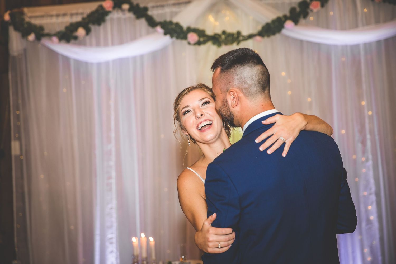 Couple sharing their first dance under twinkling lights in a rustic barn setting.