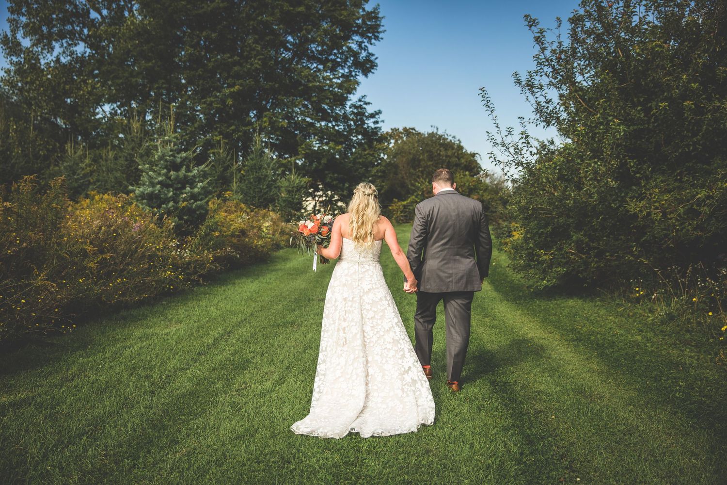 Wedding couple walks hand in hand through a green garden path on their special day.