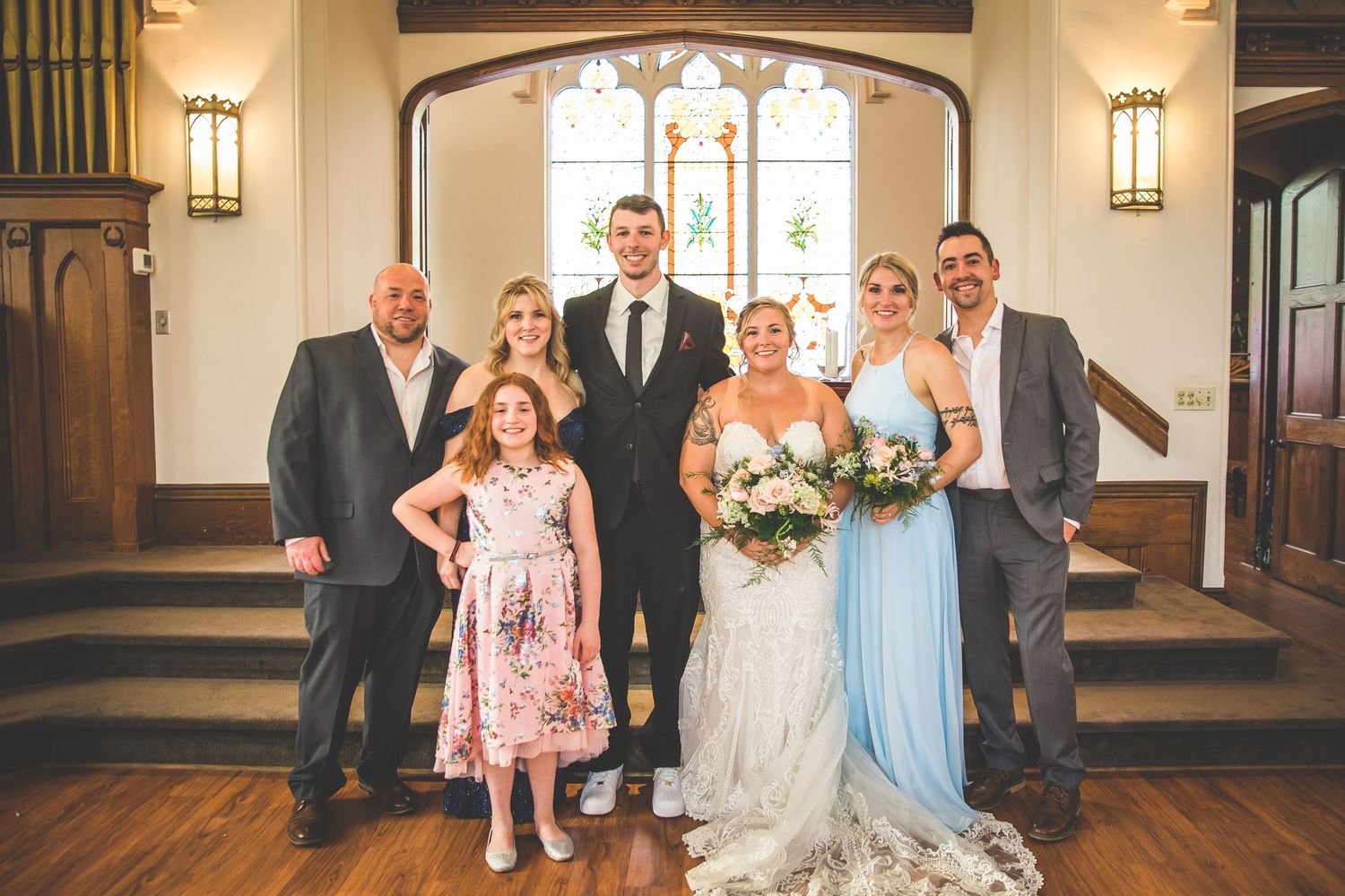 Wedding group photo in an elegant church interior with warm lighting and architectural details.