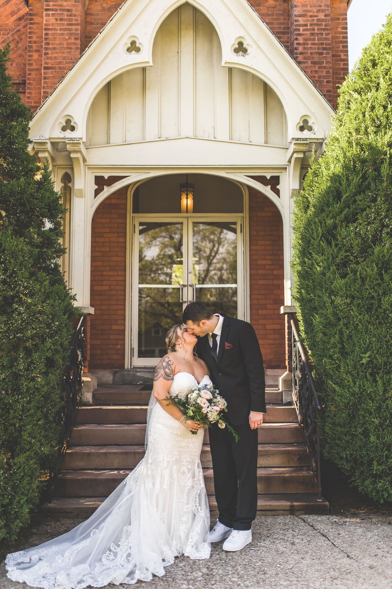 Elegant wedding portraits taken under white archway of historic brick church.