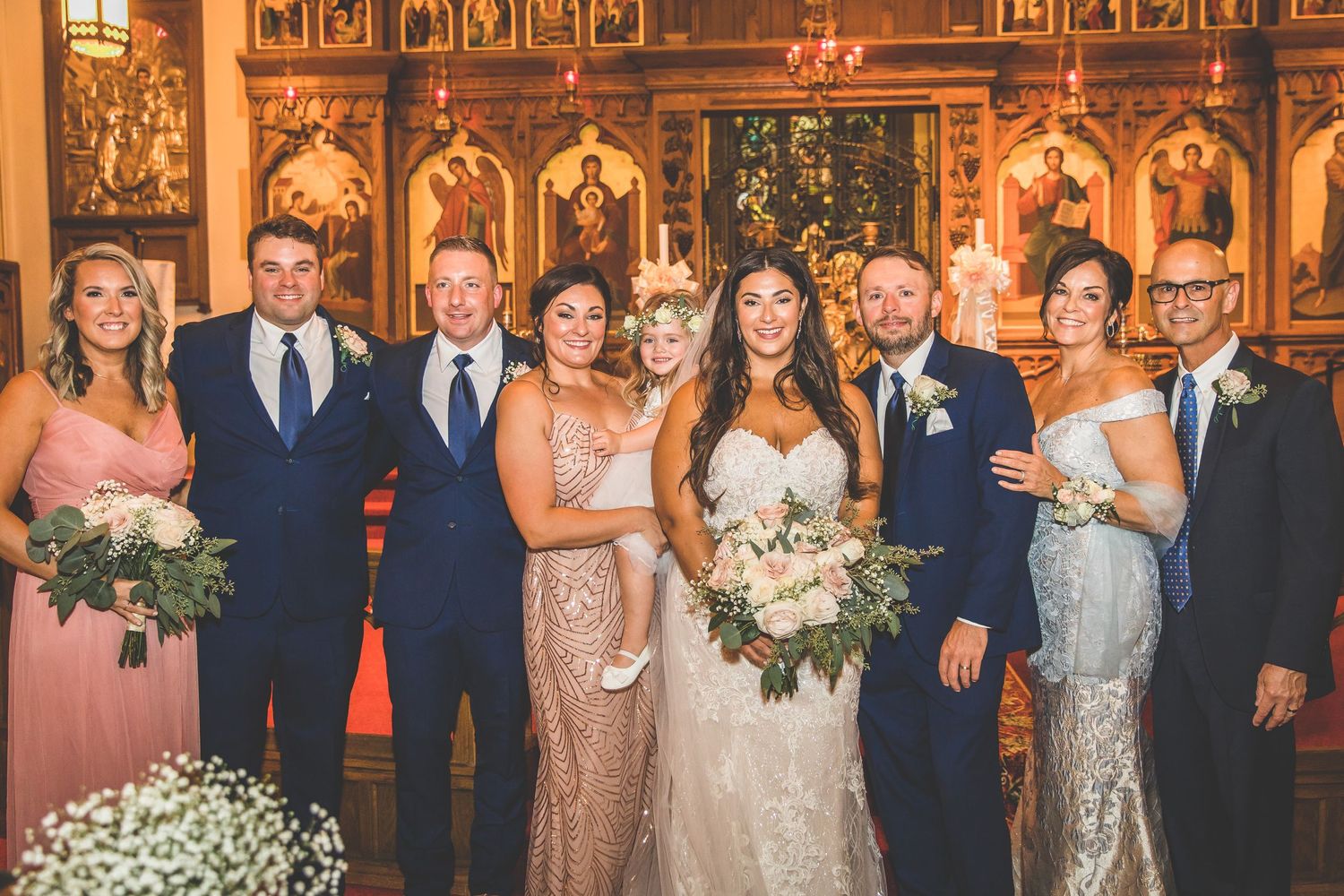 Group photo of wedding party against elaborate church altar with traditional iconography.