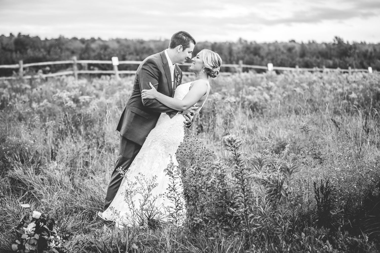 Wedding couple poses in rustic field setting for black and white portrait.