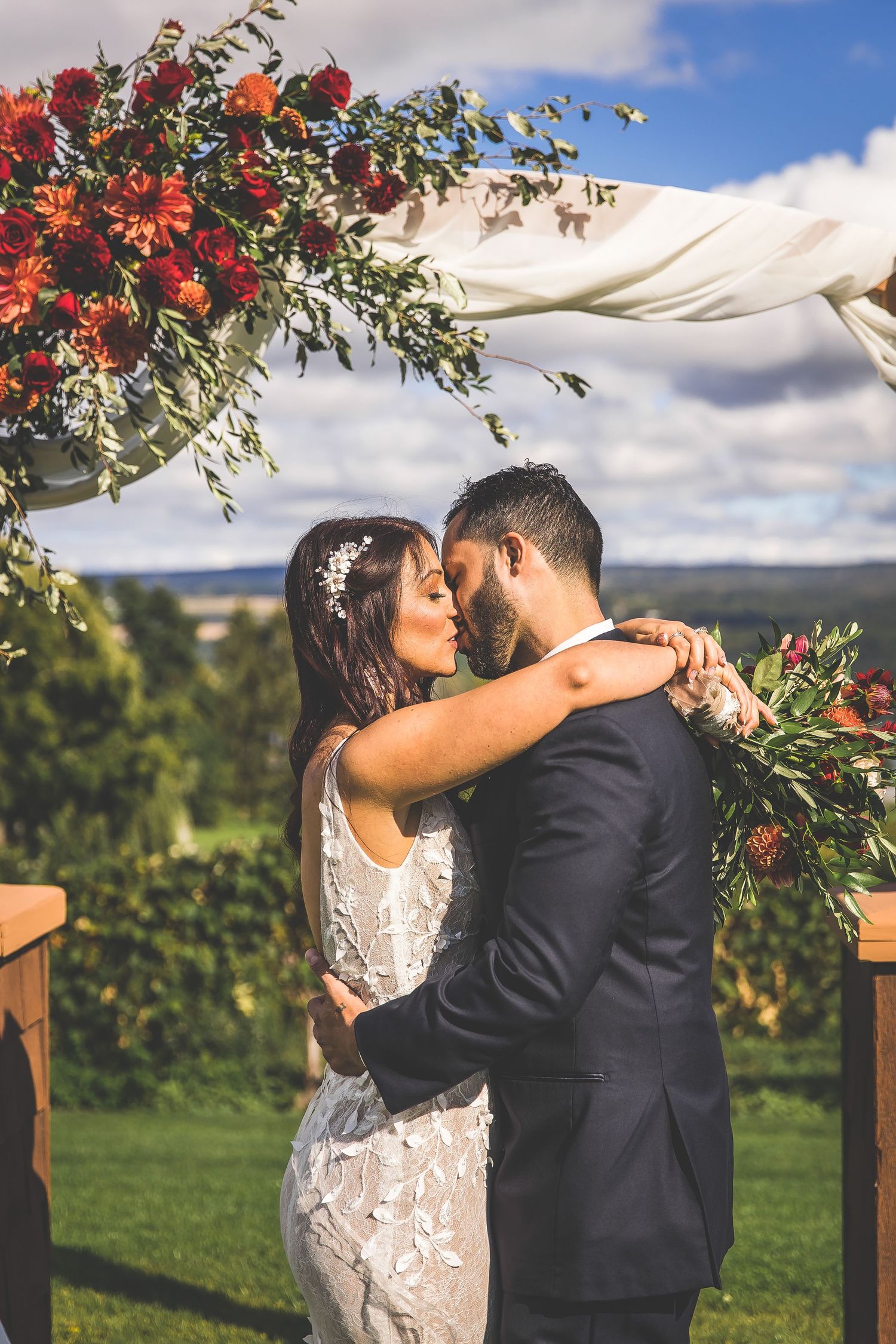 Romantic moment captured during outdoor wedding ceremony with floral arch backdrop.