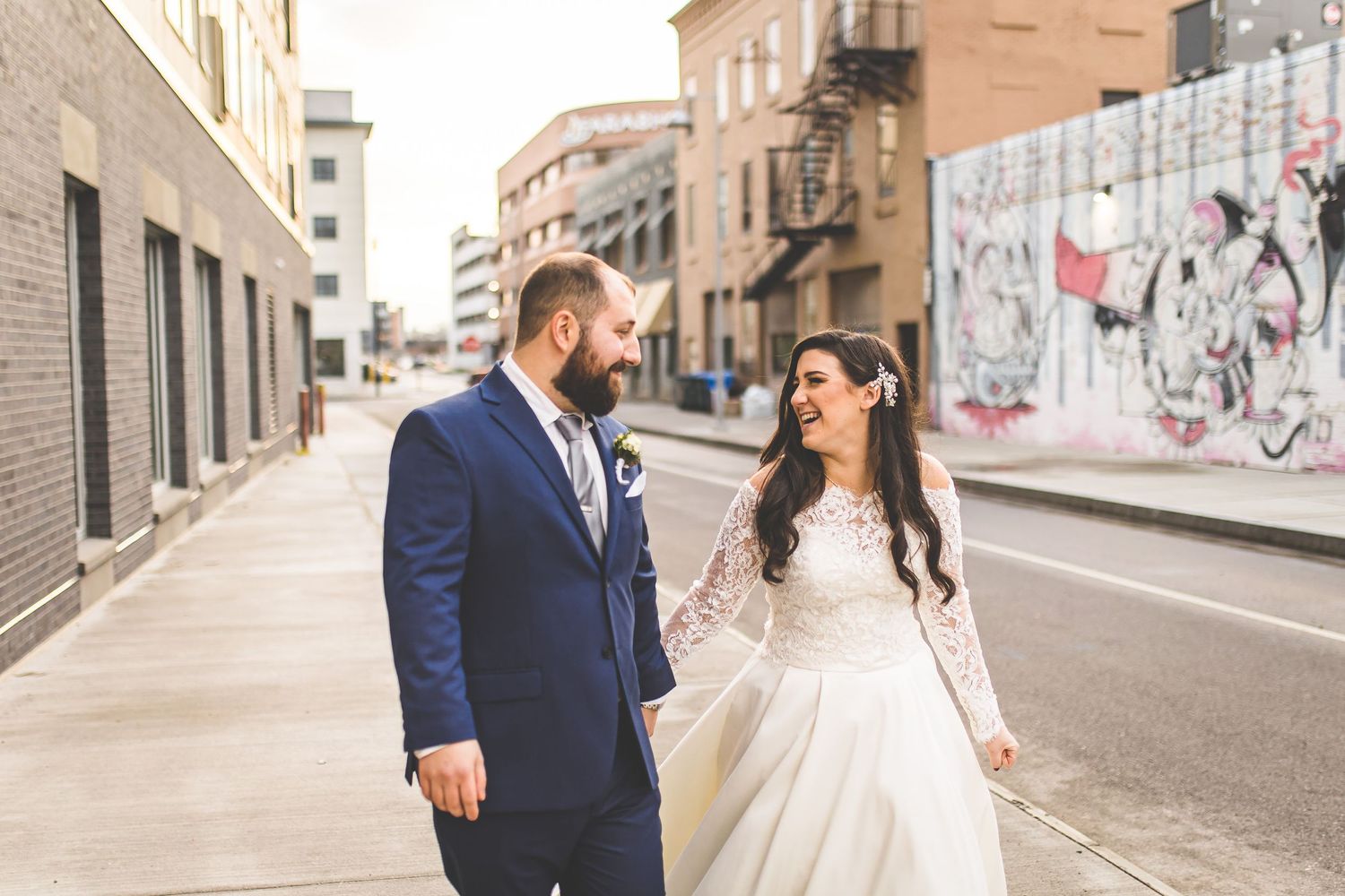 Bride and groom pose for romantic photos on an urban street with brick buildings.