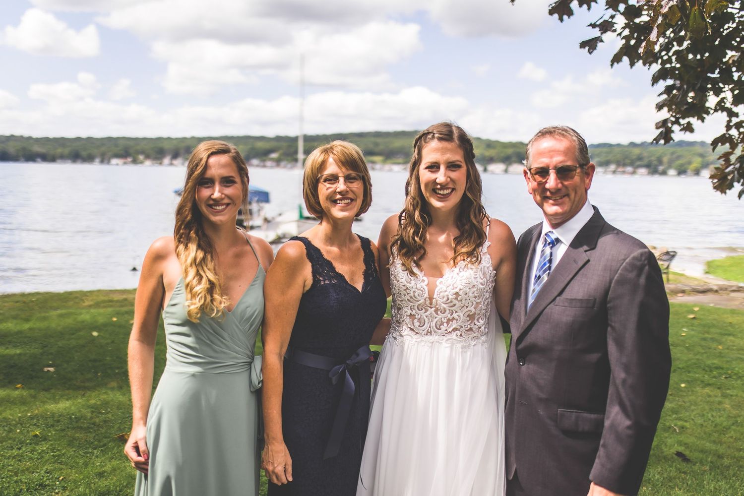 Wedding group gathers for photos by a scenic lakeside setting on a beautiful summer day.
