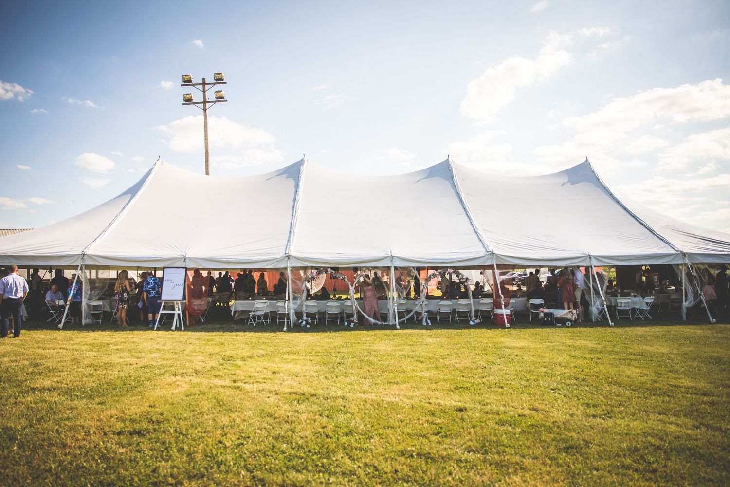 White wedding tents set up in a grassy field under blue summer sky.