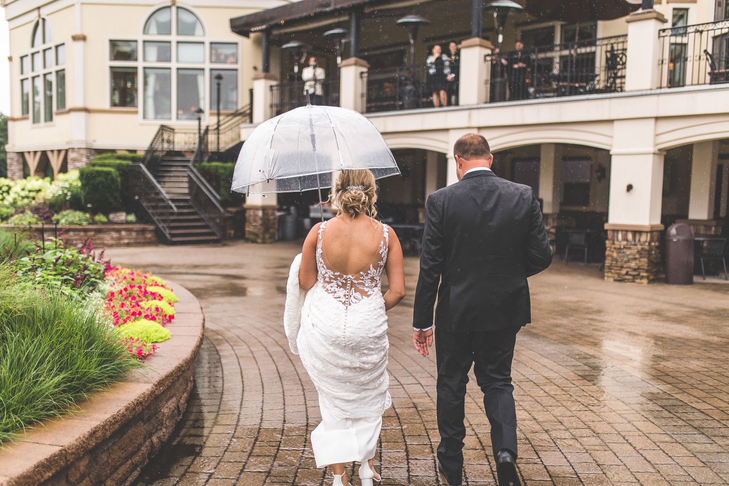 Couple walks along curved stone pathway outside elegant venue.