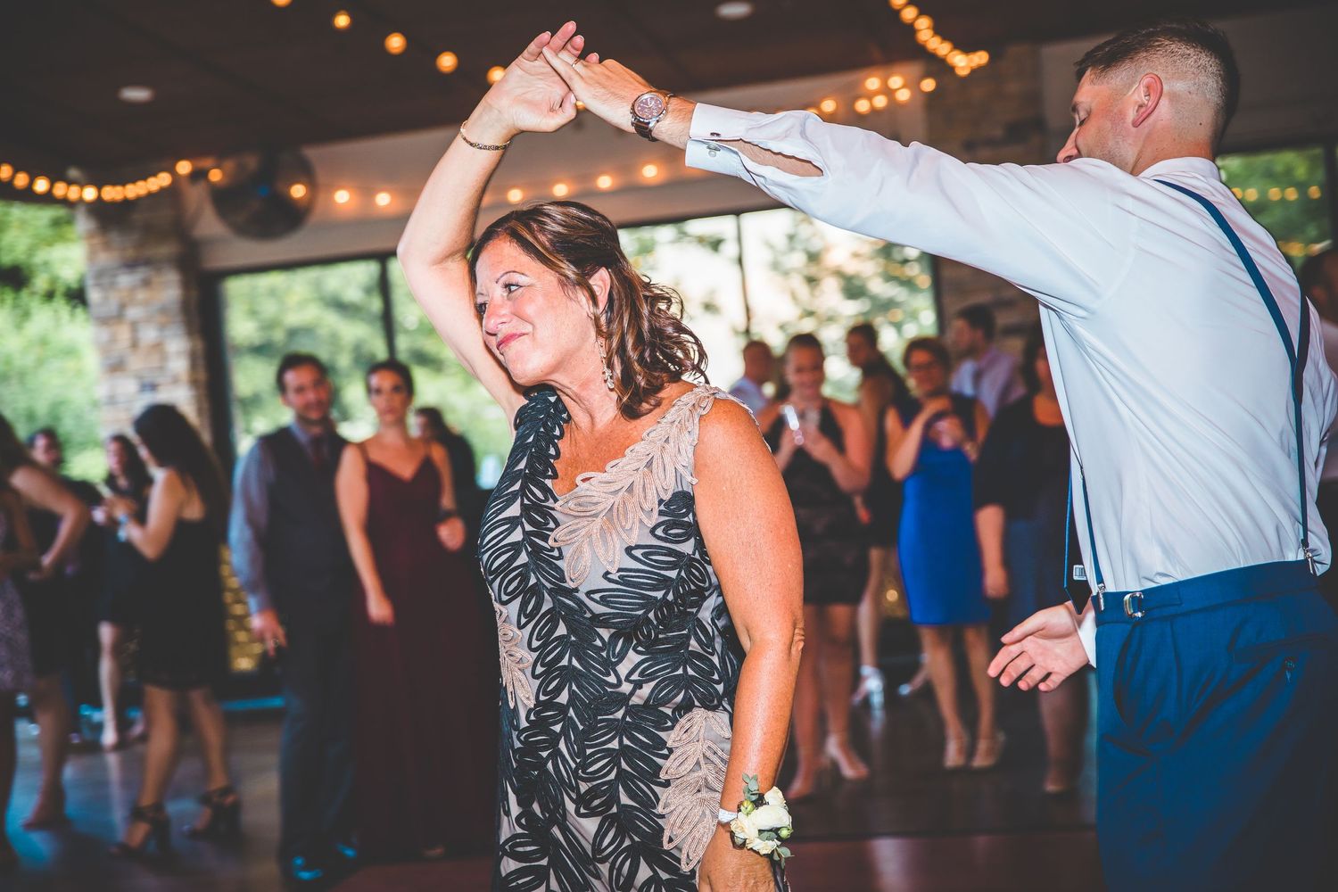 Wedding guests dancing and celebrating on a covered patio with string lights overhead.