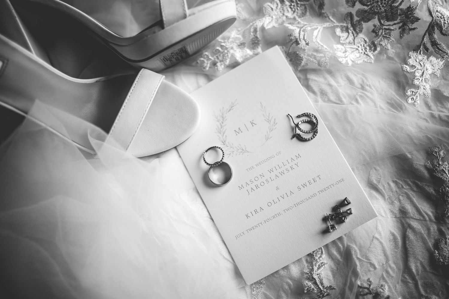 Wedding rings and invitation displayed on white feathers in black and white photography.