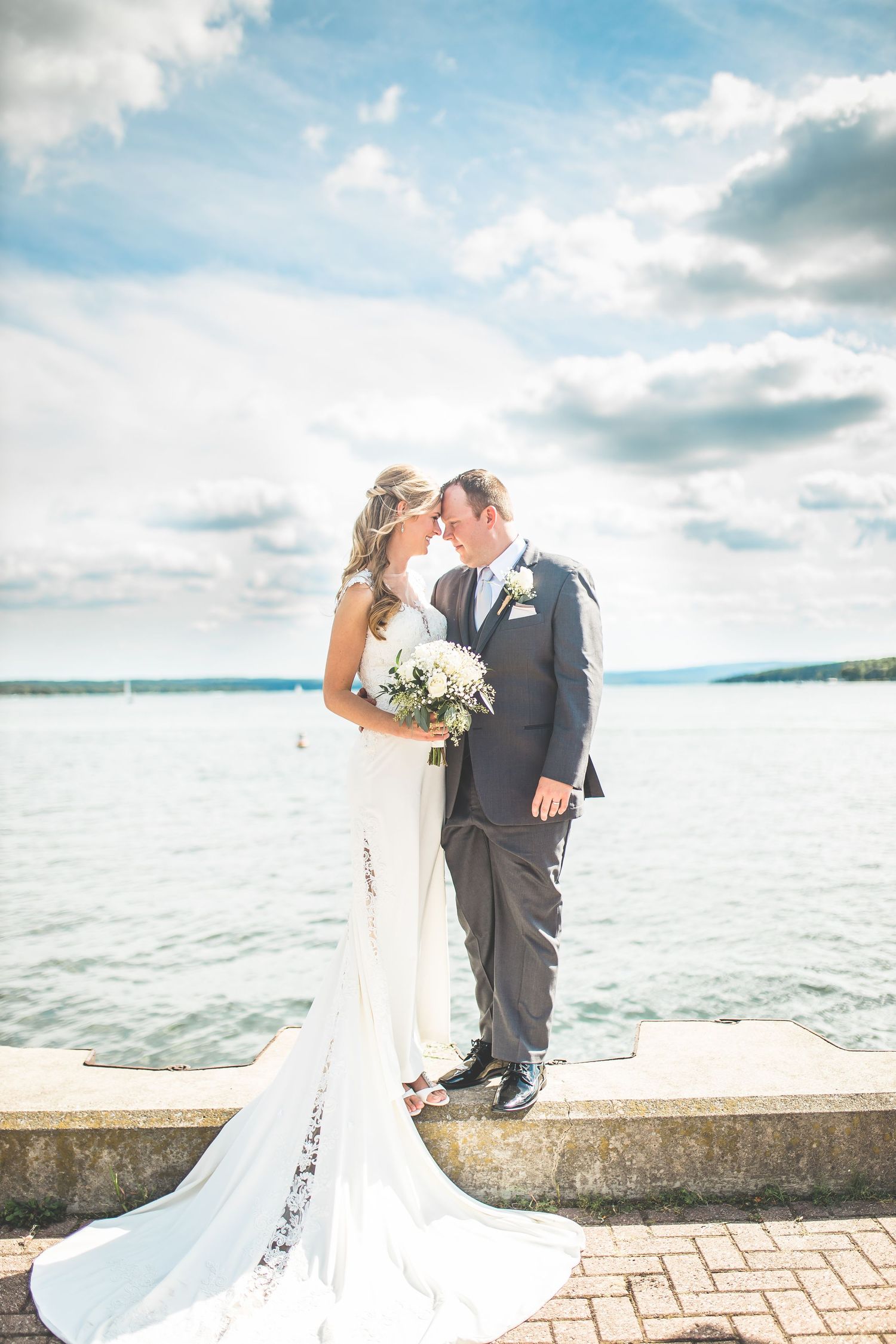 Dramatic waterfront wedding portraits with flowing dress and cloudy sky backdrop.