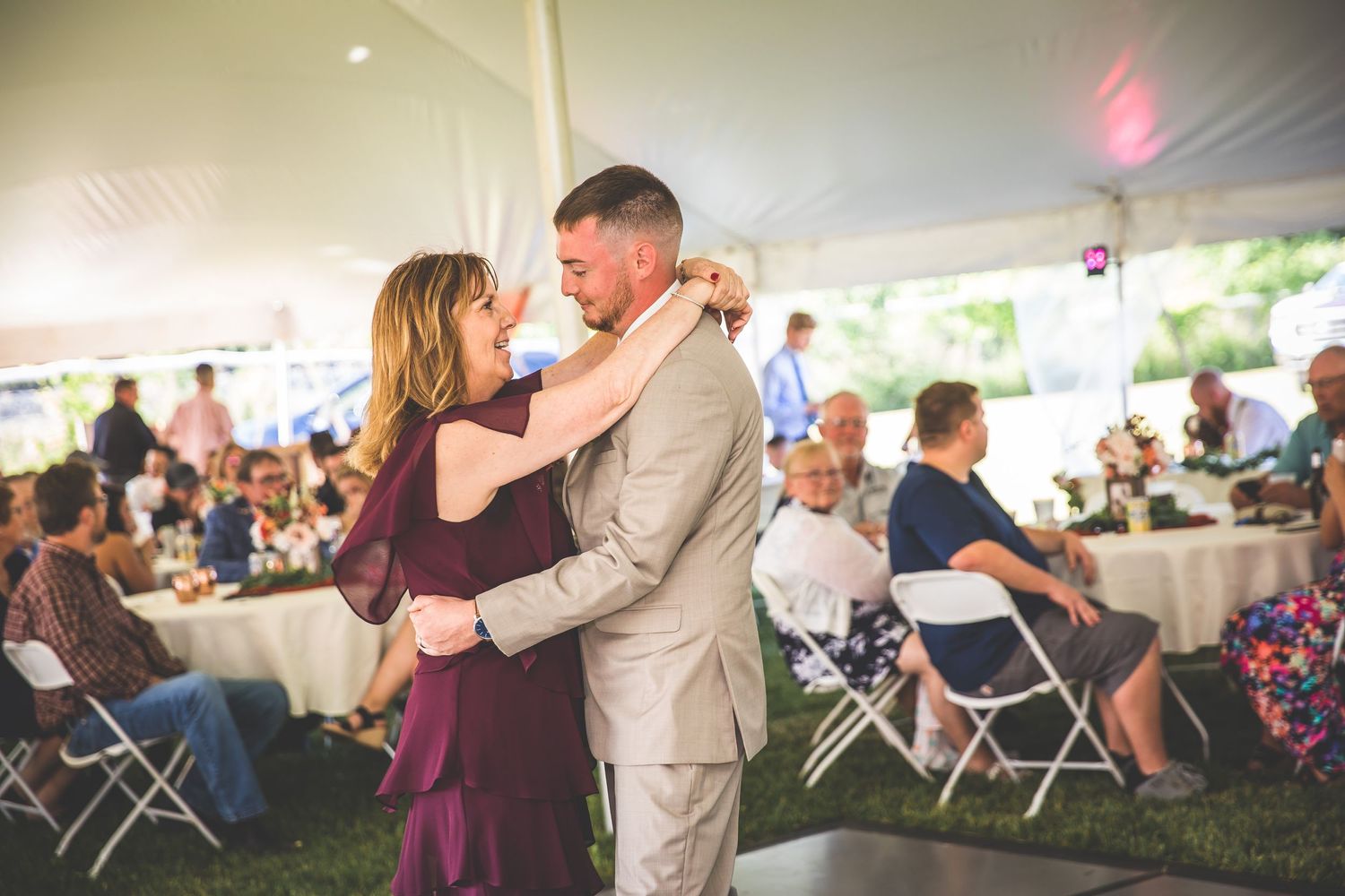 Wedding reception guests dance and celebrate under an outdoor tent with romantic lighting.
