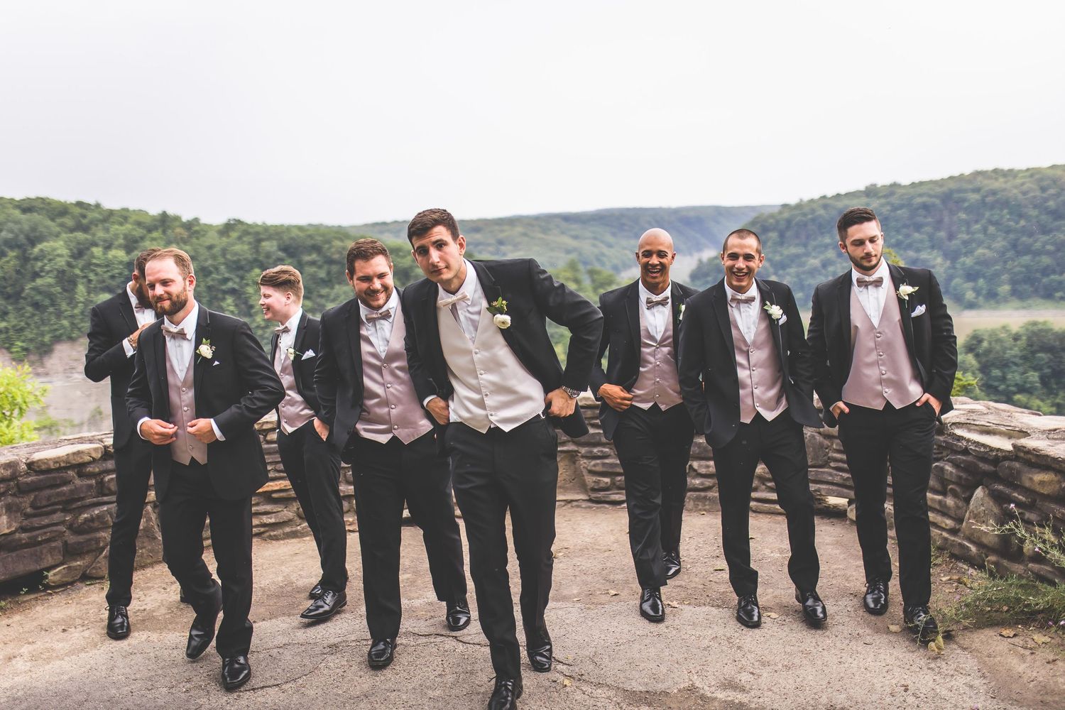 Groomsmen show off their dress shoes in a fun lineup photo against a stone wall with mountain views.