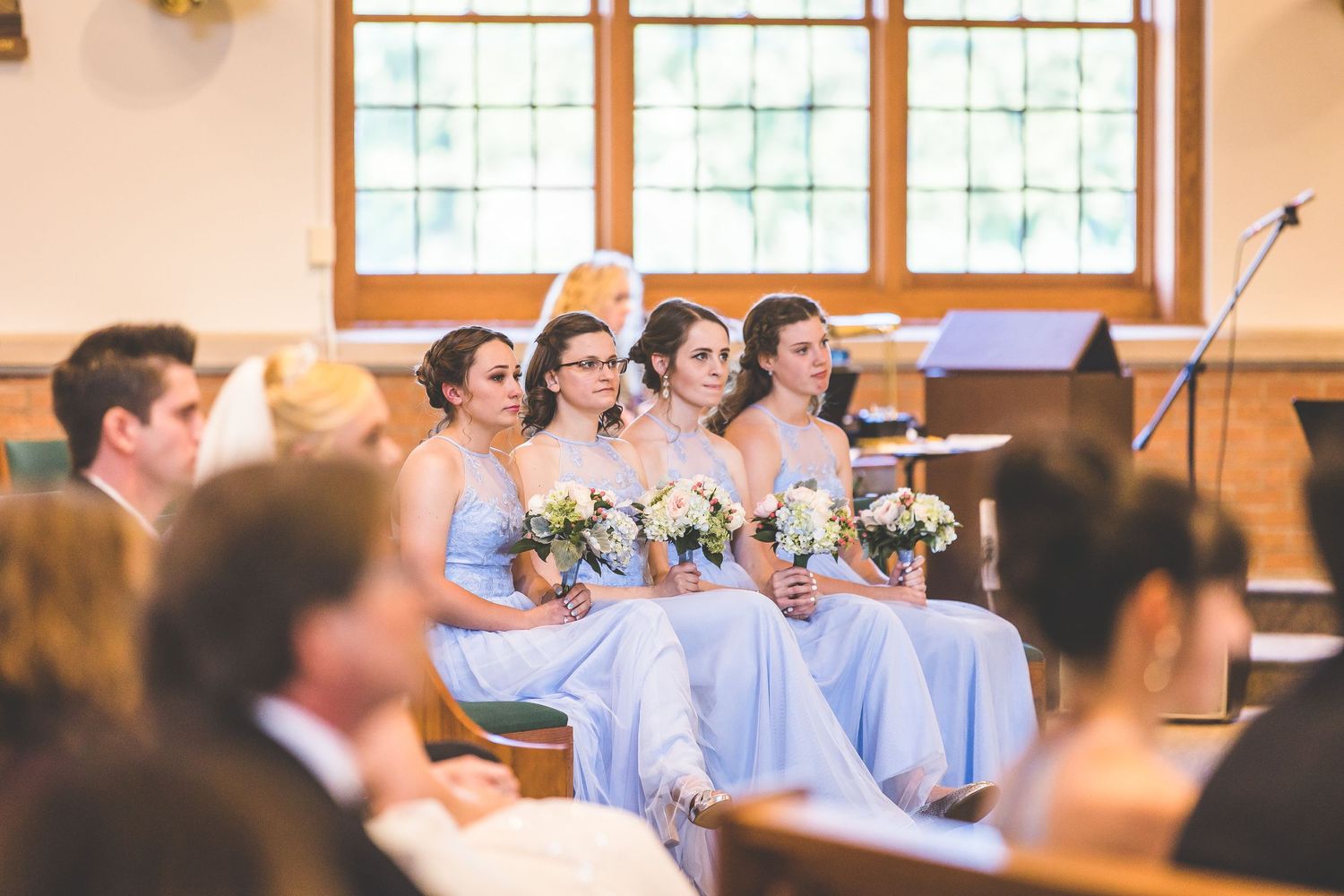 Church interior with wooden pews and bridesmaids in light blue dresses.
