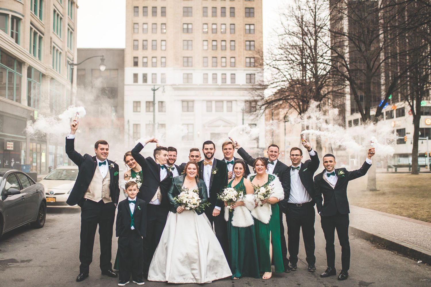 Joyful wedding party celebrates outdoors in winter with urban skyline backdrop.