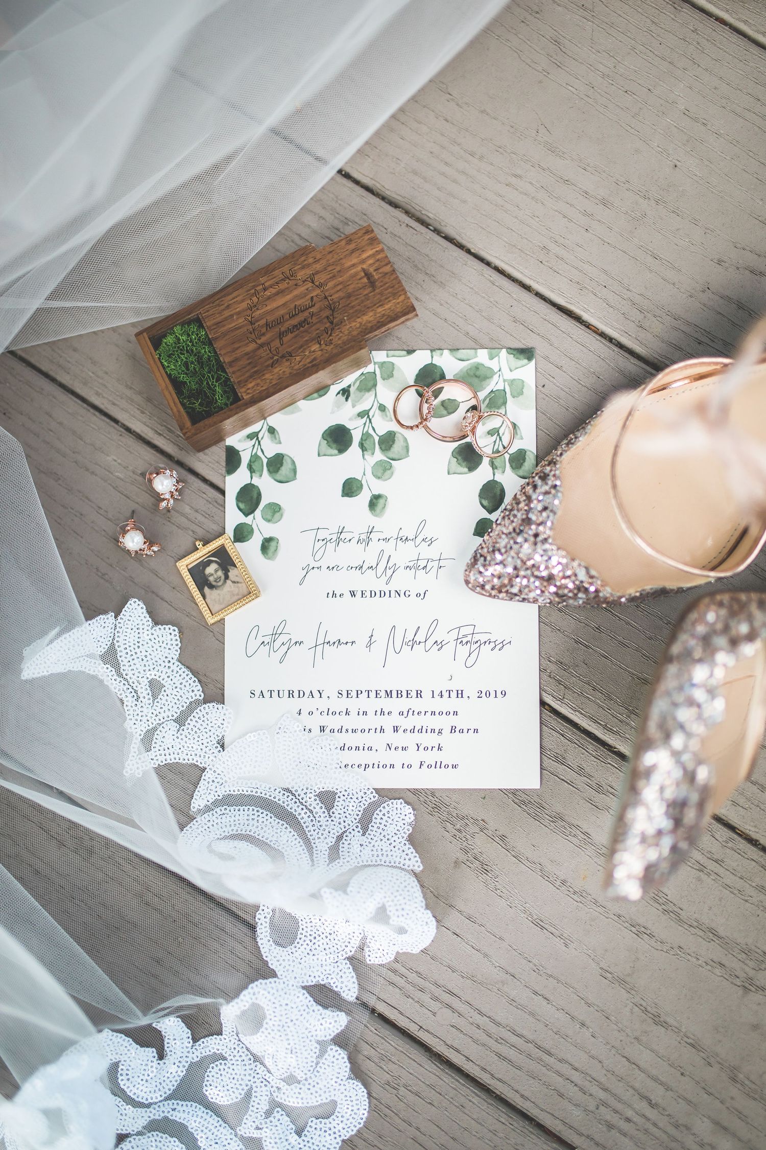 Wedding invitation with eucalyptus design and lace veil on wooden surface.