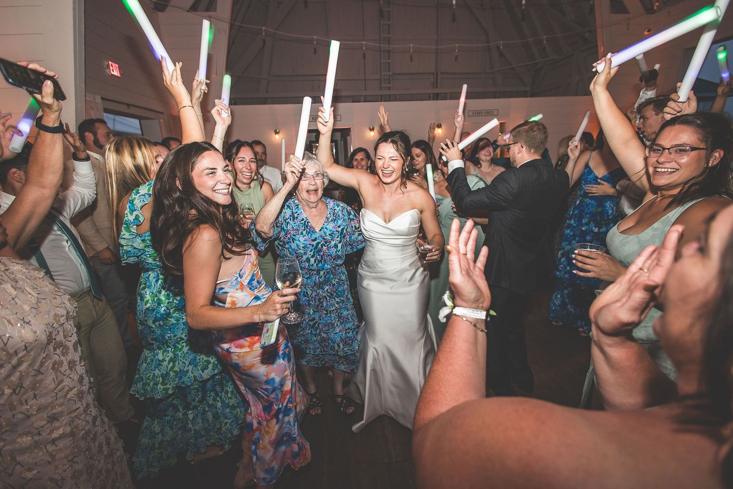 Wedding guests wave glowing light sticks while dancing at a reception celebration.