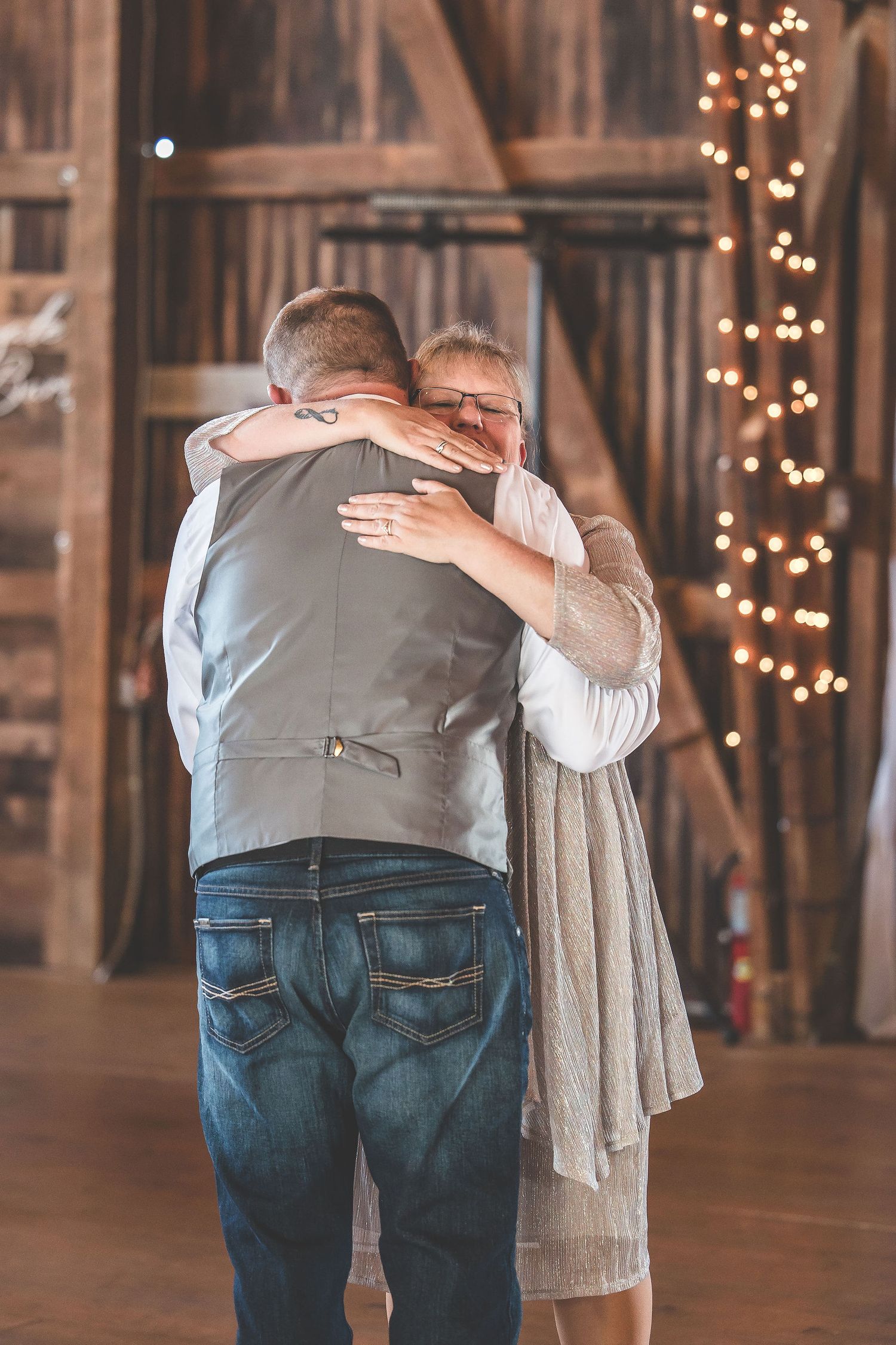 Dancing couples in a rustic barn wedding venue with romantic string light ambiance.