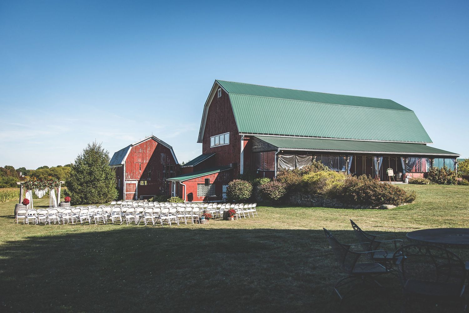 Panoramic view of a countryside farm with red barns and green fields under blue skies.