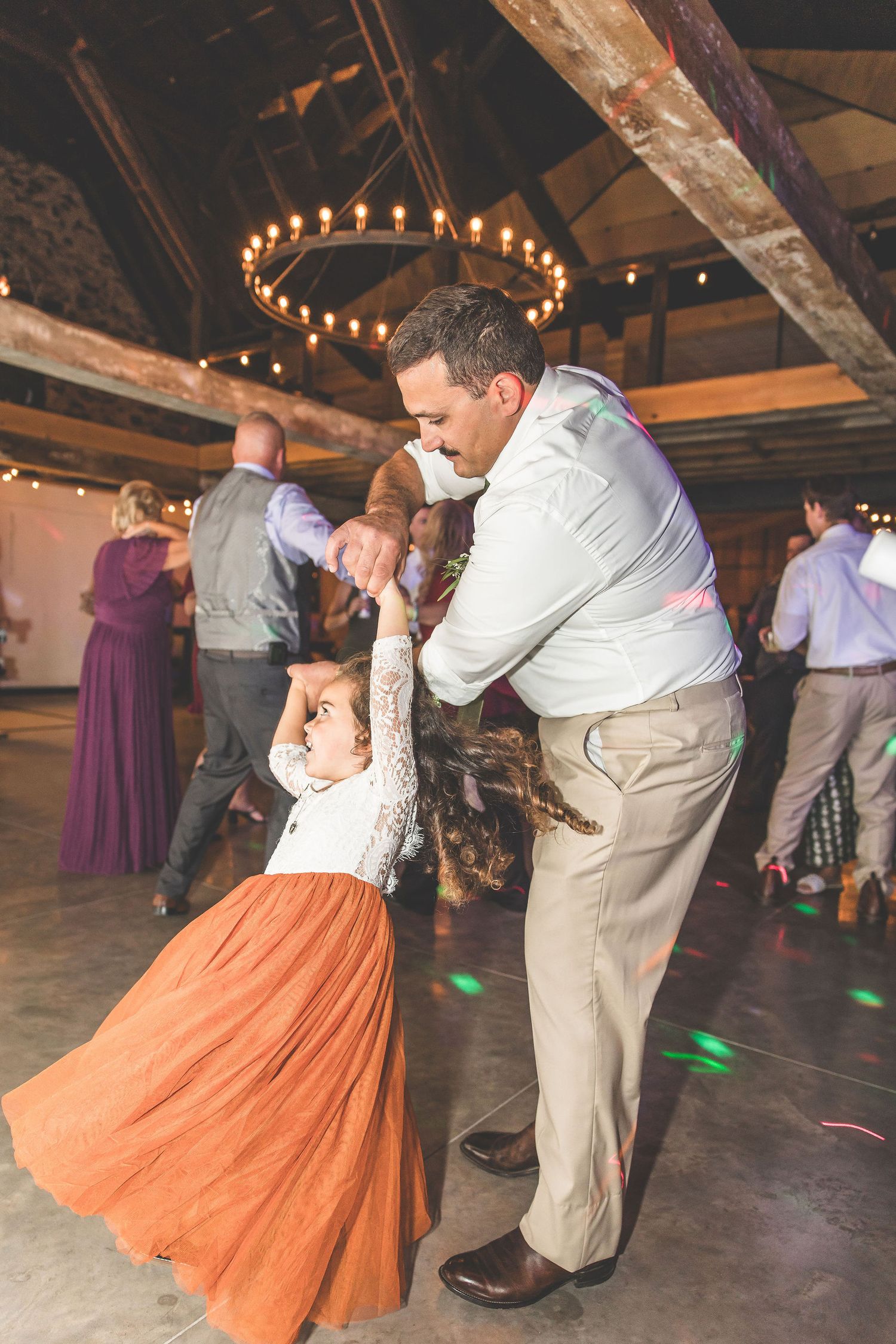 Couples dance together at a rustic venue with string lights overhead and wooden beams visible.