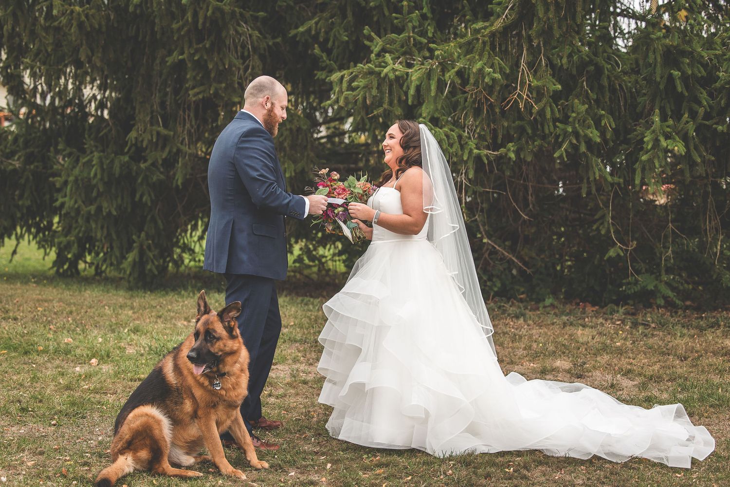 A couple shares a special moment during their woodland wedding with their German Shepherd nearby.