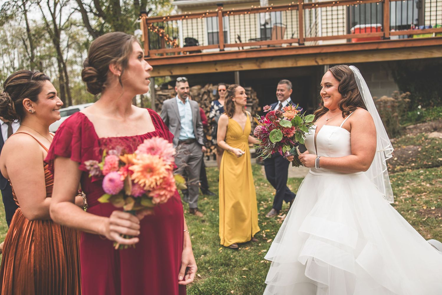 Wedding party in burgundy and yellow dresses poses outdoors during fall ceremony.