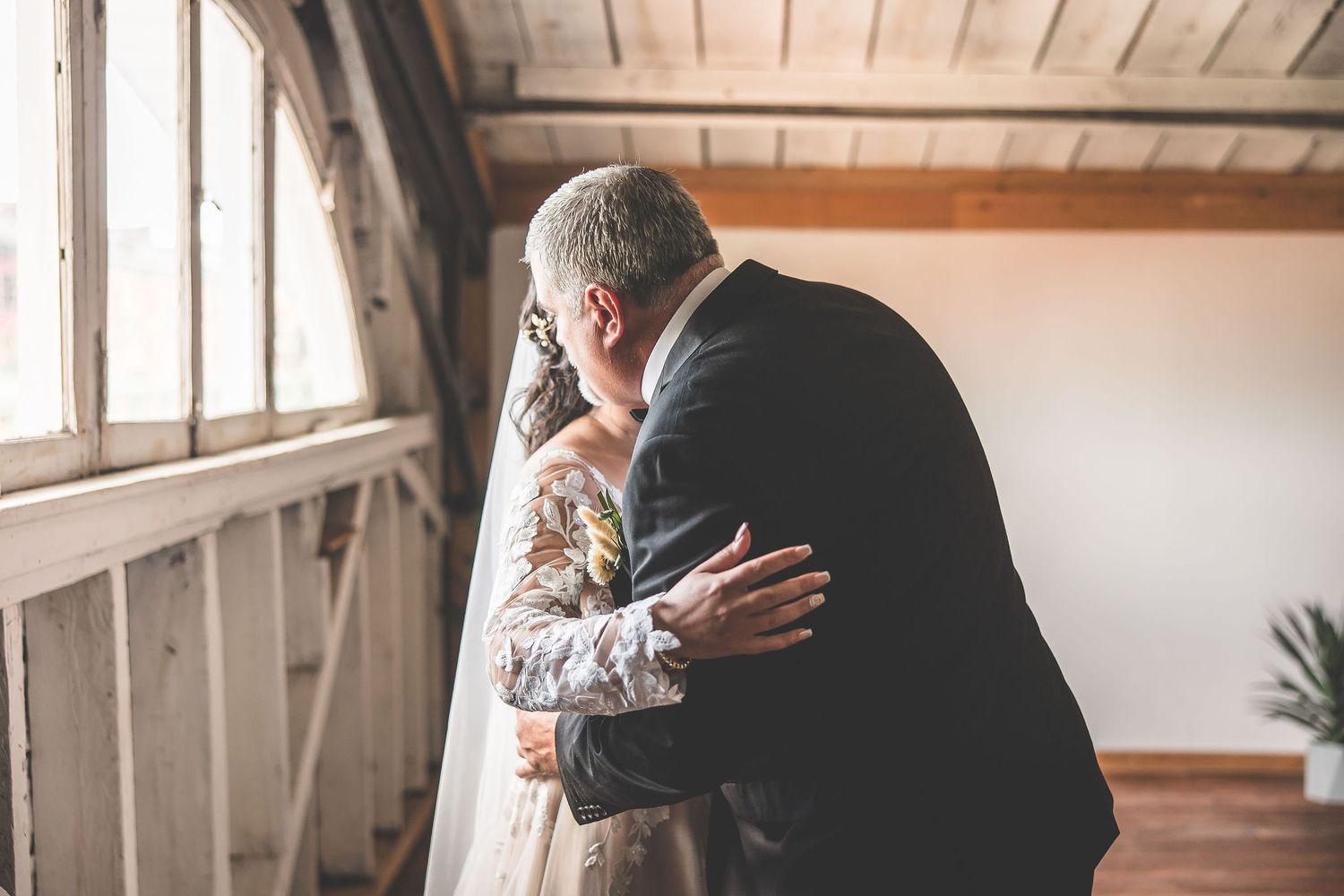 Wedding party gathers in a rustic venue with wooden ceiling beams and natural light.