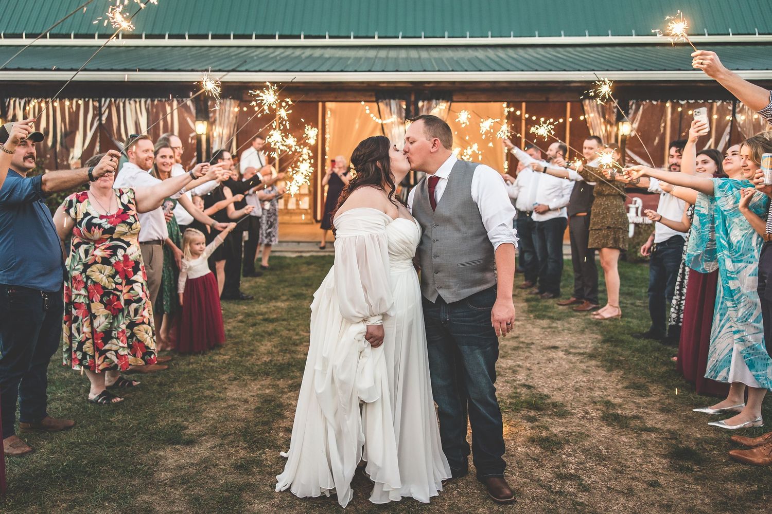 Wedding celebration outdoors with guests gathered around a rustic barn venue.