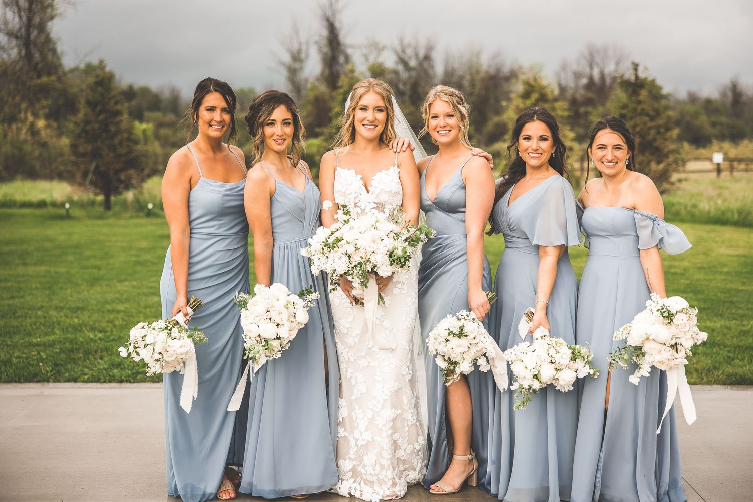 Bridal party in powder blue dresses poses with bouquets on outdoor patio.