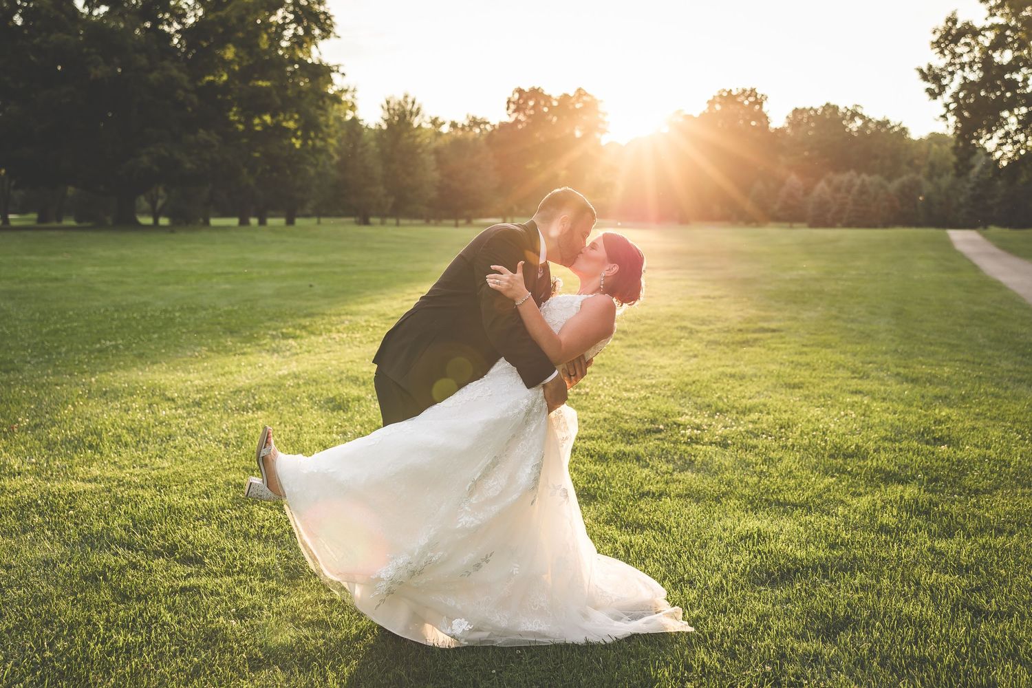 Newlyweds share an intimate moment on a grassy lawn during sunset.