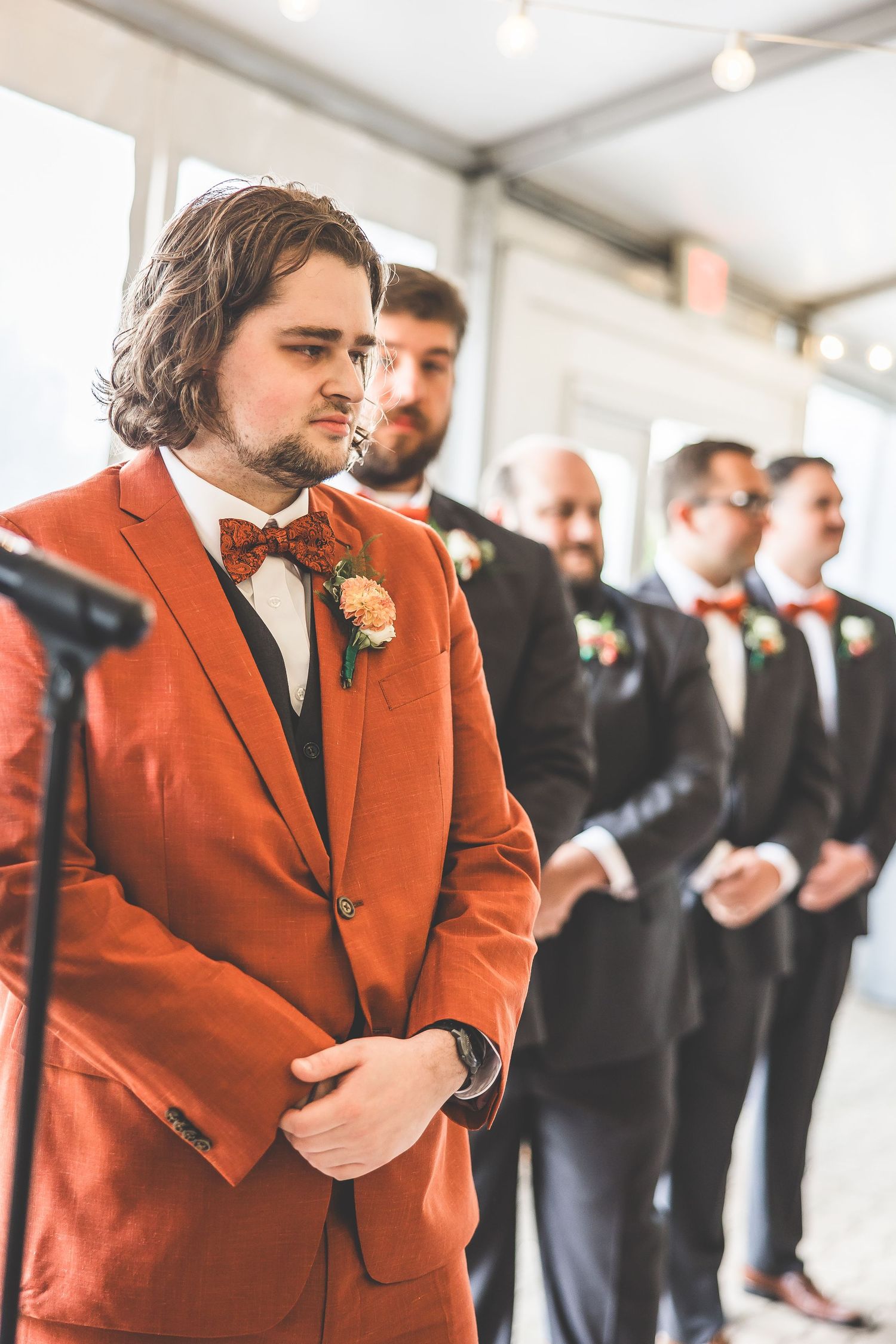 Wedding party members stand in line wearing rust-colored suits and black formal attire.