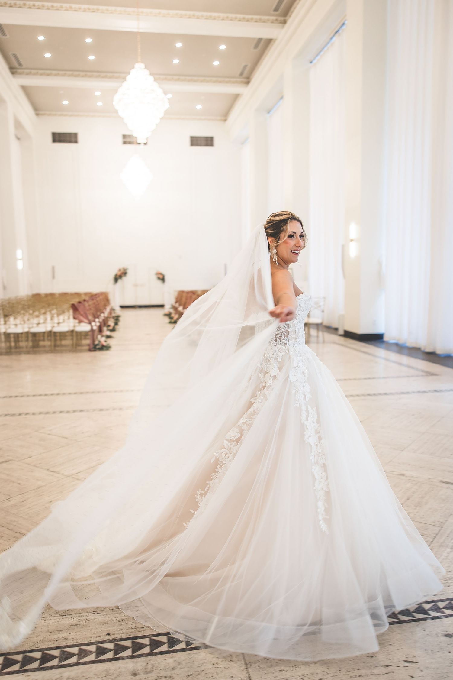 Elegant bride in flowing white ballgown twirls and dances in spacious white reception hall.