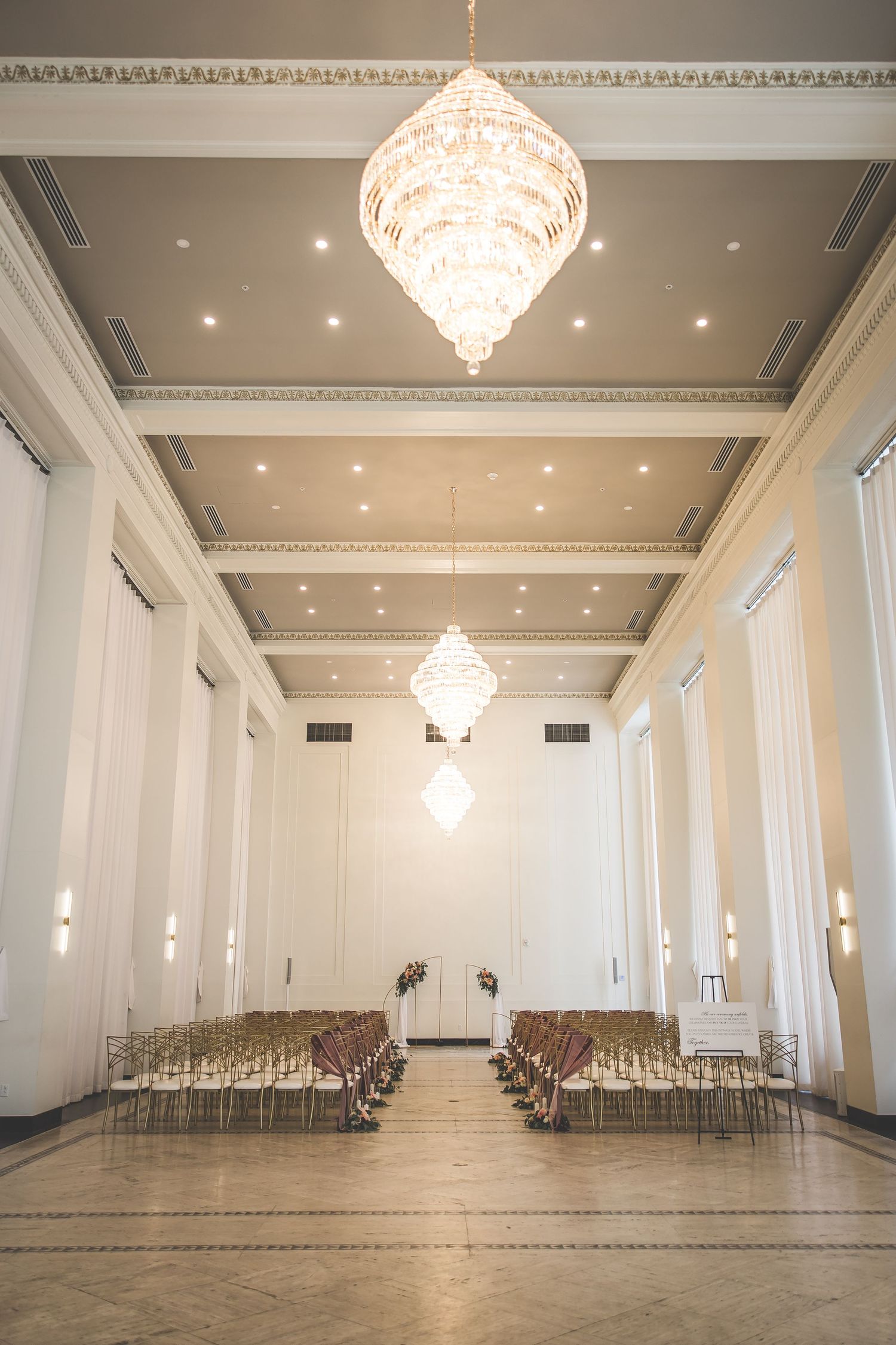 Empty elegant ballroom with crystal chandeliers and white columns.