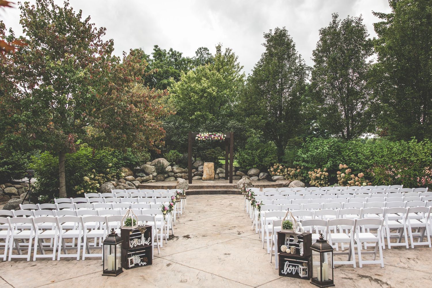 Outdoor wedding ceremony setup with white chairs and rustic wooden arch.