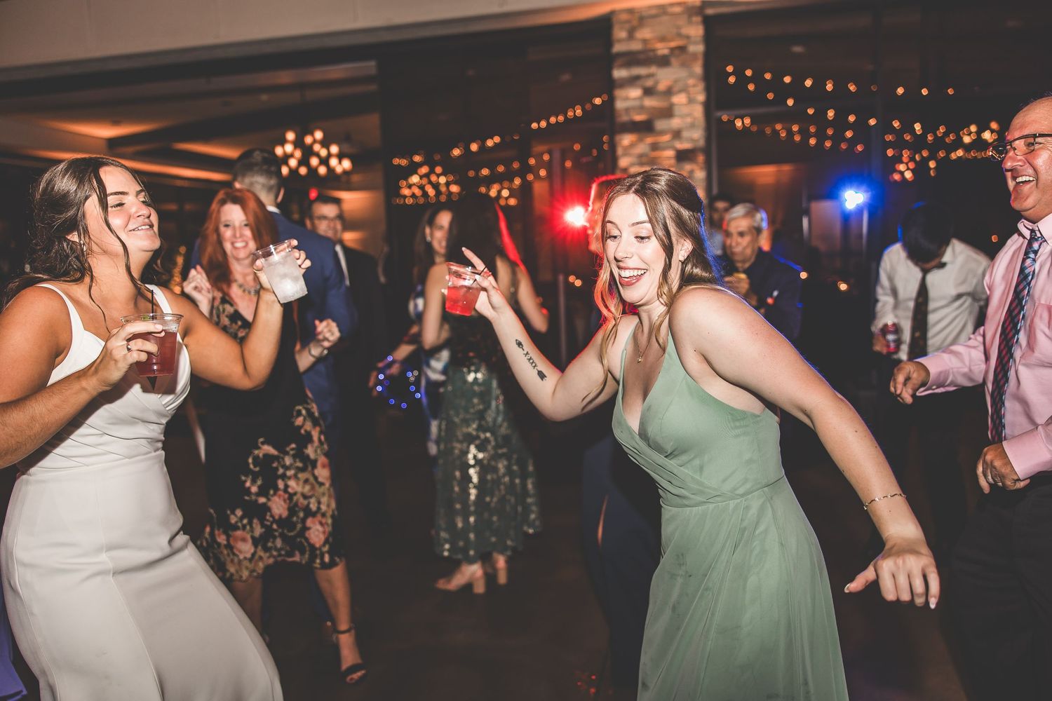 Wedding guests dancing and celebrating in a venue decorated with string lights.
