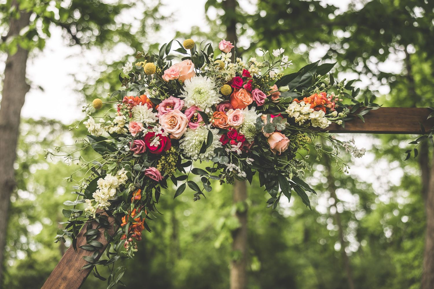 Beautiful floral arch arrangement with pink, white and coral flowers against a blurred green outdoor background.