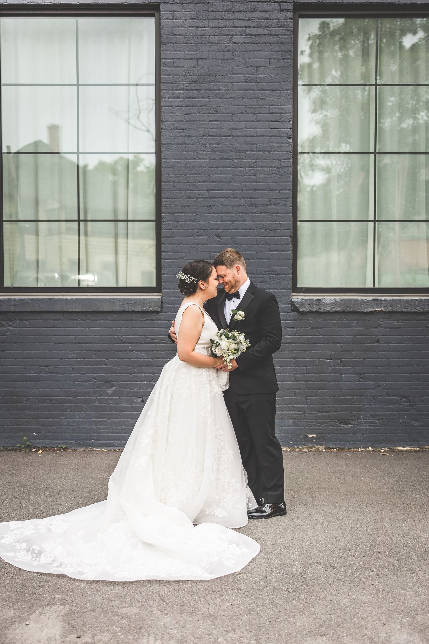 A romantic wedding moment captured against an industrial backdrop with dark brick walls.