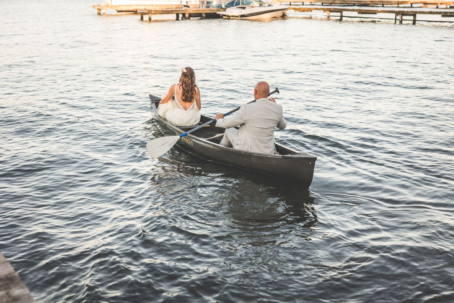 Wedding couple rowing away in small boat on lake during sunset.
